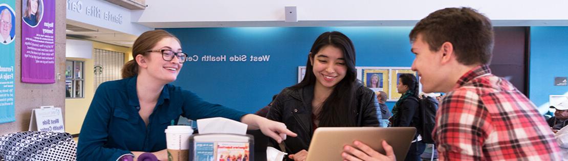 Students look at a computer and chat in a student lounge area